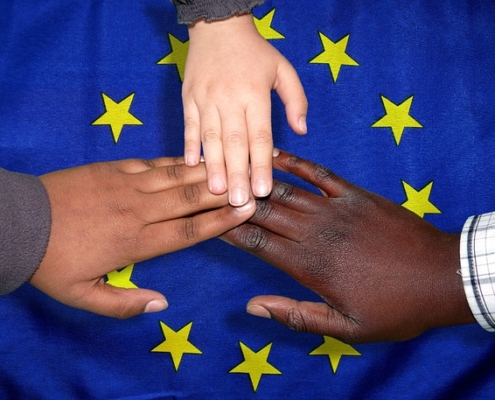 Menschen verschiedener Hautfarben legen ihre Hände zusammen über der EU Flagge um eine Einigung zu zeigen.