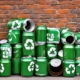 Many green cans with recycling symbols are stacked up in front of a wall symbolizing the new recycling goals.